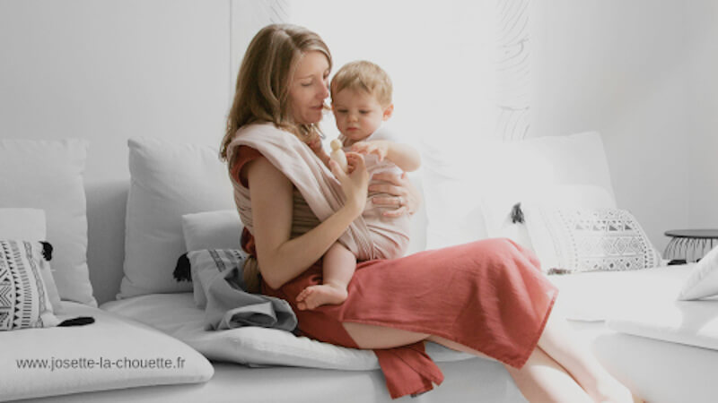eine Frau, die ein Kind mit einem Babytragetuch trägt