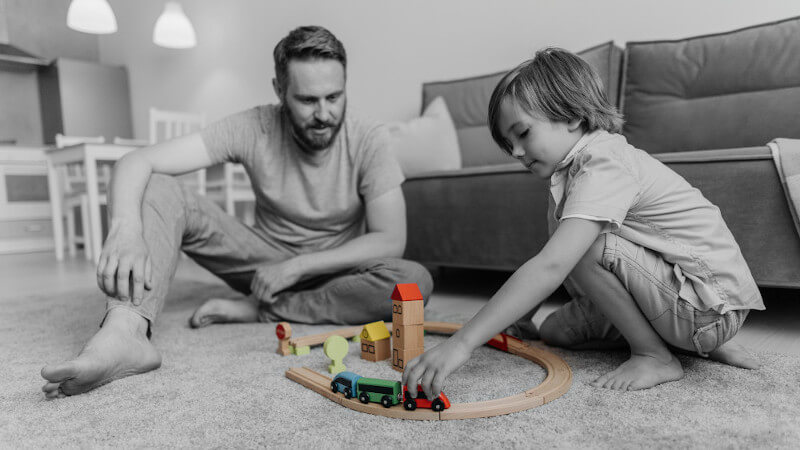 un papa qui joue avec son fils avec des jouets train en bois