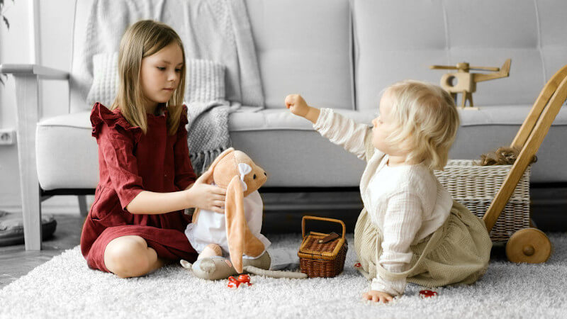 zwei junge mädchen, die mit puppen spielen