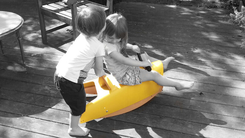 zwei kinder, die mit einem hölzernen schaukelpferd spielen